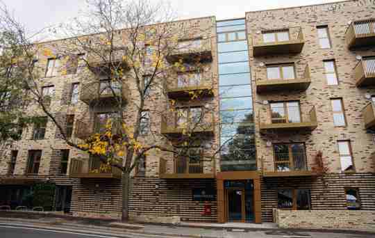 Bath House external view facing the road with balconies and a large tree with yellowing leaves