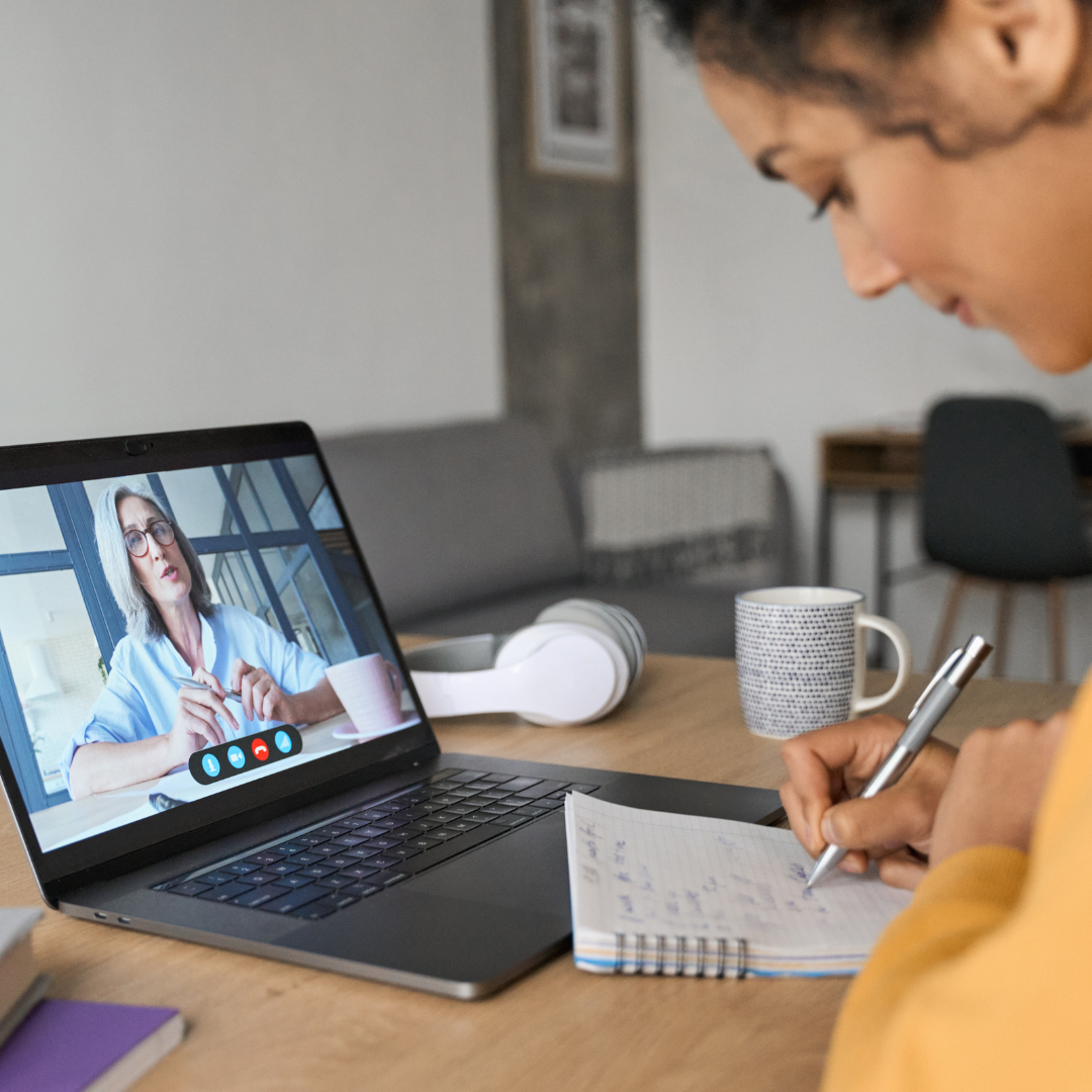 Person writing on a notepad in front of laptop
