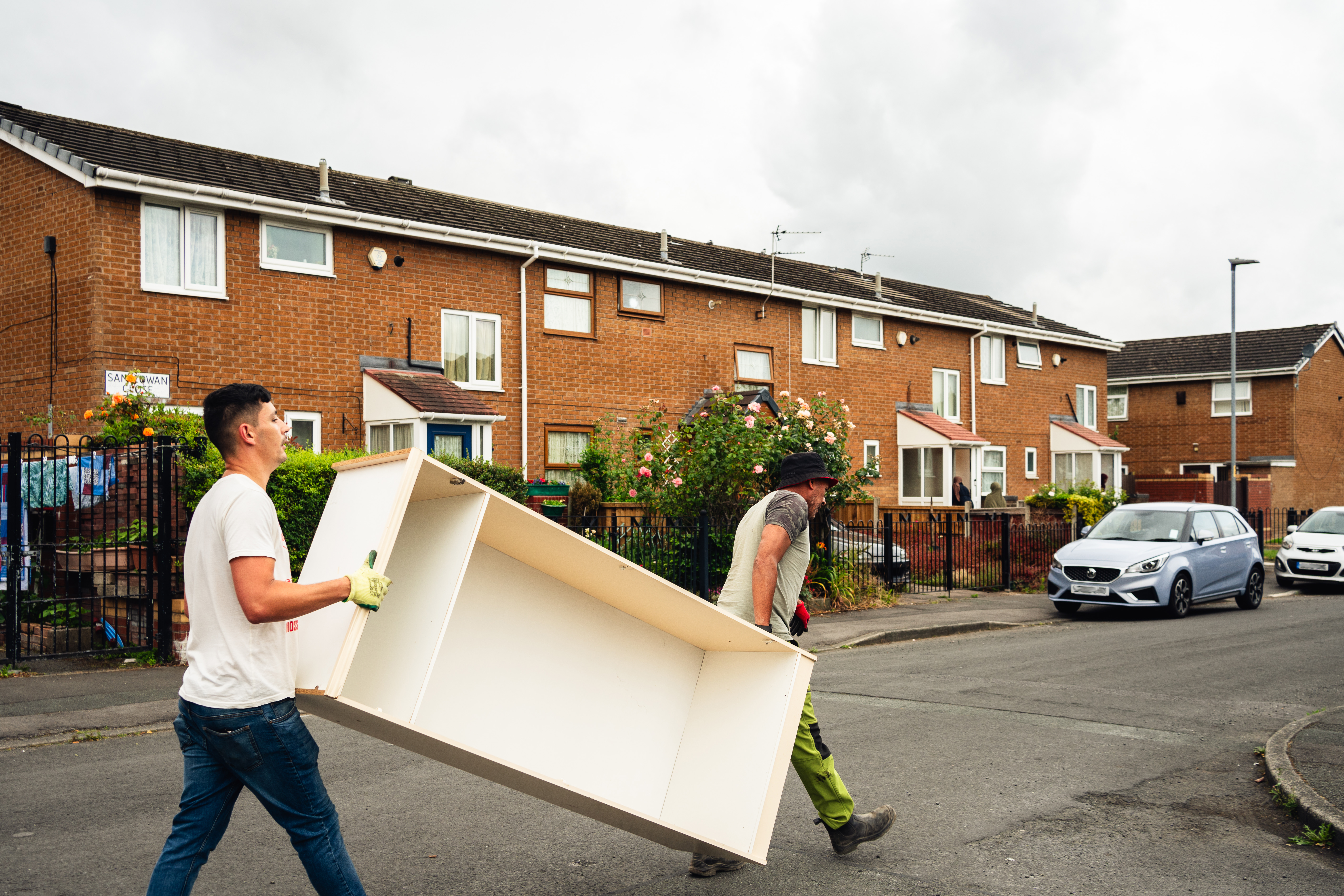 Two people carrying a piece of furniture down a street